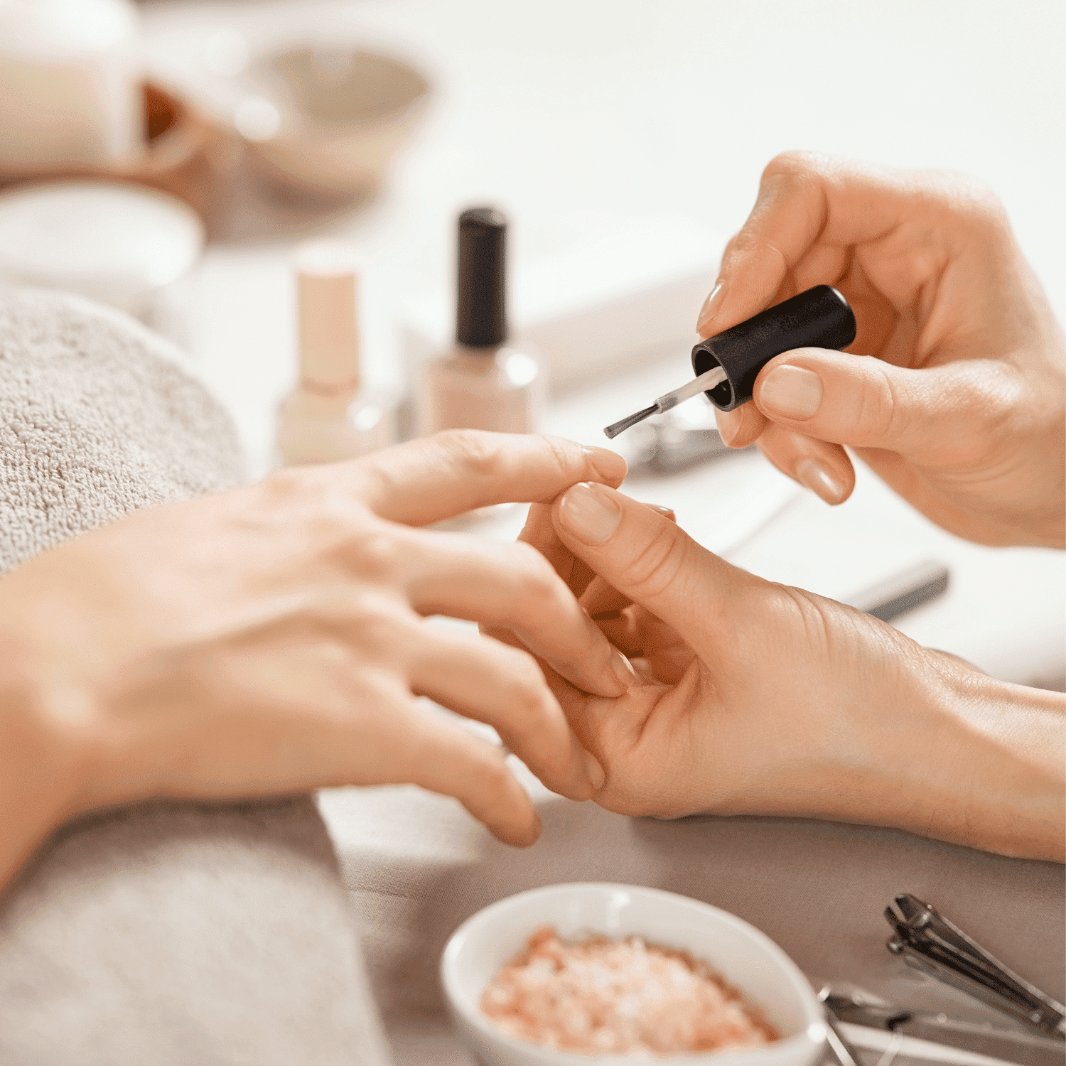 Nail technician applying polish to client's fingernails, with manicure tools nearby.