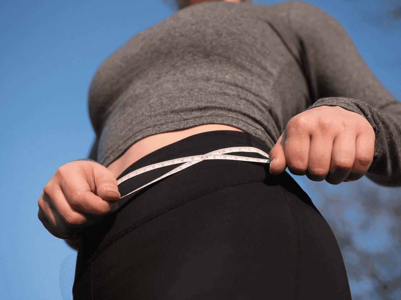 Person measuring waist with tape in a health or fitness context.