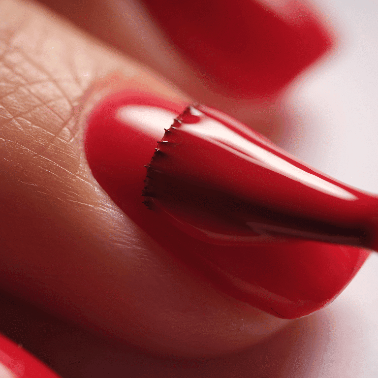 Close-up of a fingernail being painted with glossy red nail polish.