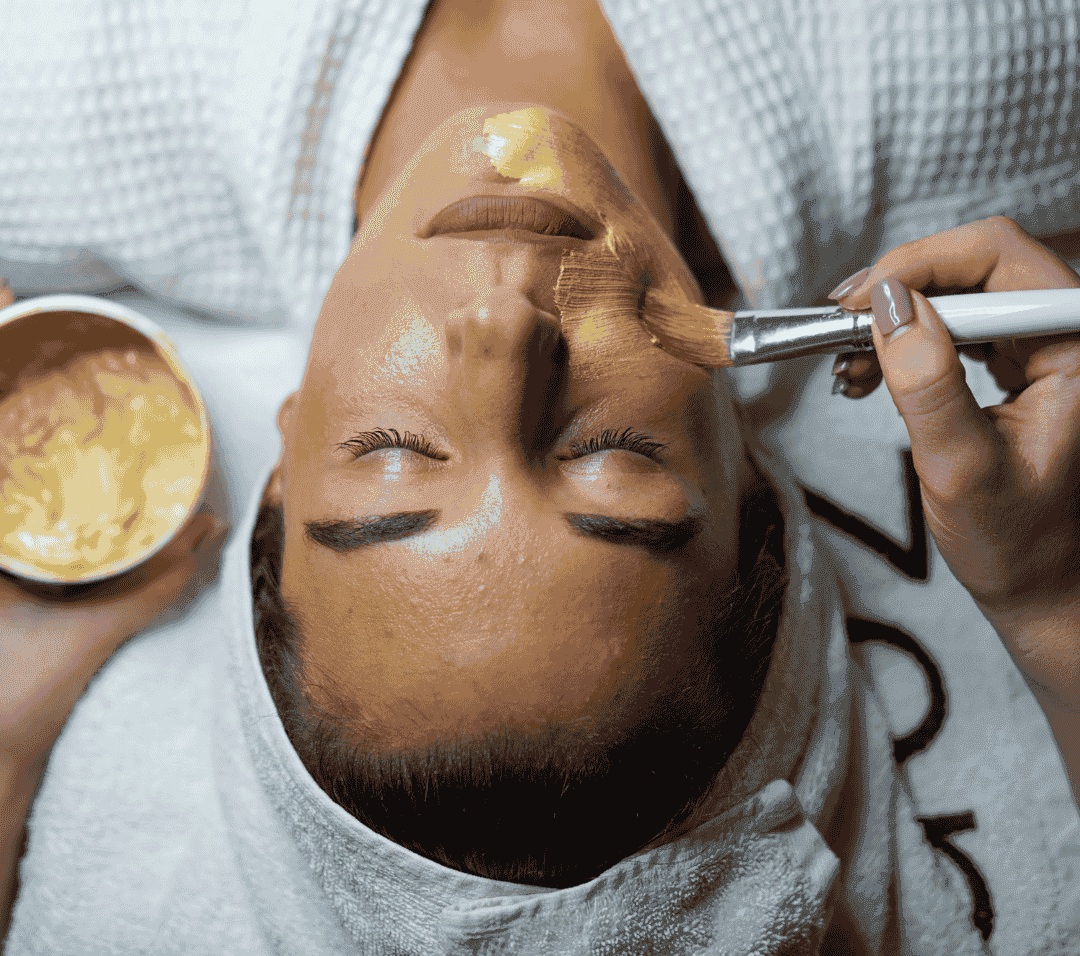 Facial treatment with golden mask applied by brush in spa setting.